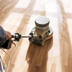 En person slipar ekparkett med en maskin. Dammet virvlar upp från golvet.