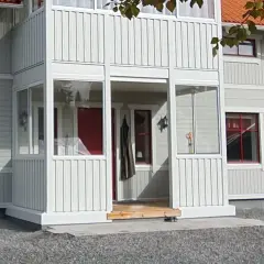 Nybyggd farstukvist med vita träpaneler och glaspartier. En röd ytterdörr syns innanför.