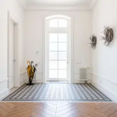 Vacker hall med mönstrat golv och en stor glasdörr. Ett paraplyställ med gula och svarta paraplyer står till vänster.