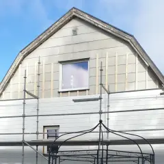 Hus med eternit fasad under renovering, ställningar uppsatta.