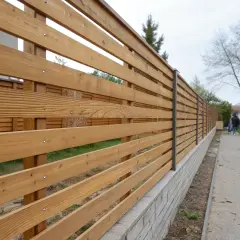 Ett modernt staket med liggande ribbor i olika bredd, monterat på en låg mur.
