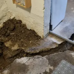 Hål i betonggolvet visar på pågående arbete med att laga rör. Jord och sten ligger uppgrävt vid väggen.