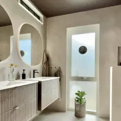 Modernt badrum med dubbla handfat och speglar. Väggarna har en slät, betongliknande finish, liknande microcement på kakel, vilket ger en lyxig och enhetlig känsla.