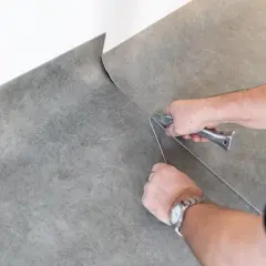 Händer som använder en mattkniv för att laga plastmatta.