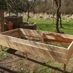 En nybyggd odlingslåda av virke står på gräsmattan, redo att fyllas med jord för sommarens projekt.
