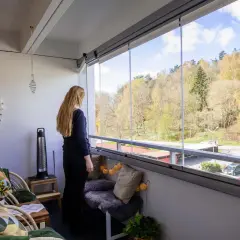 En kvinna njuter av utsikten från en mysig, inglasad balkong. Perfekt liten balkong inspiration med korgstolar och en sittbänk.