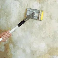 Handen putsa grovt grus på en vägg med en slipmaskin.