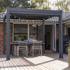 Man pratar i telefon vid ett bord under en modern pergola med vasstak. En laptop står på bordet.