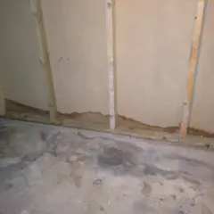 Synlig fukt i garage vid golvet och längs väggen. Vattenfläckar på betongen och mörka märken på väggens nederkant.