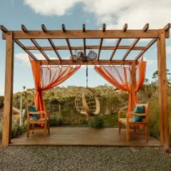 En träpergola med orange draperier och hängstol. Perfekt för avkoppling, kanske efter att ha fått pergola bygglov.