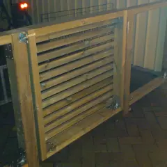 En nybyggd grind med liggande ribbor i trä, fäst med metallbeslag.