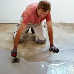 Man med spackel breddar ut grått material på betonggolv. Undrar du över slipa betonggolv pris?