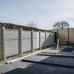 Ett nytt staket runt tomtens gräns byggs. Material ligger redo för montering.
