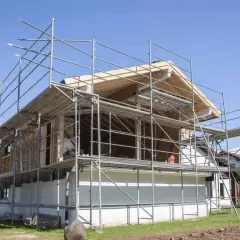 Bygga på en våning: Ställningar omger ett hus under ombyggnad, med synliga träbjälkar och takkonstruktion.