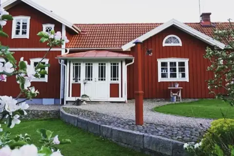 Rött hus med vita fönster och dörrar, en vacker trädgård med blommande träd. Planer på att bygga ut gammalt hus syns inte, men det ser ut som ett drömhem.