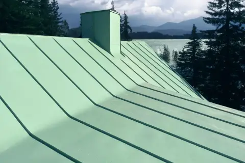 Grönt plåttak med skorsten, vacker utsikt över sjö och berg. Tänk på kostnad plåttak vid renovering.