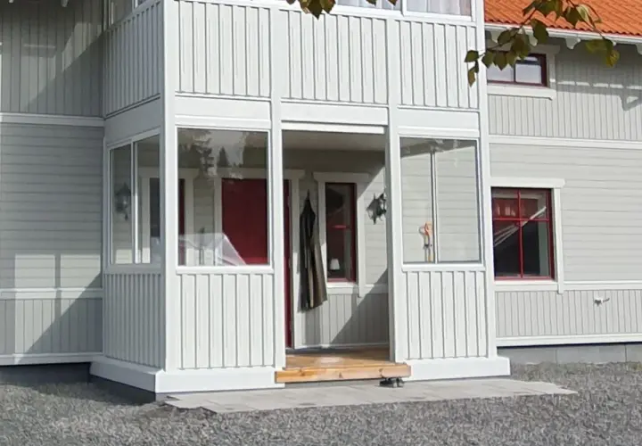 Nybyggd farstukvist med vita träpaneler och glaspartier. En röd ytterdörr syns innanför.