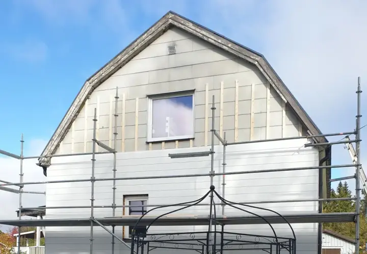 Hus med eternit fasad under renovering, ställningar uppsatta.
