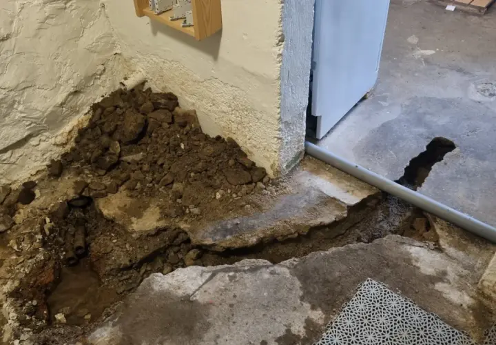 Hål i betonggolvet visar på pågående arbete med att laga rör. Jord och sten ligger uppgrävt vid väggen.