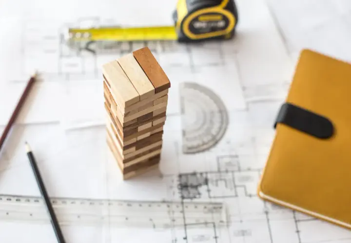 Ritningar, måttband, pennor och en Jenga-torn som symboliserar planeringen för att renovera garage.