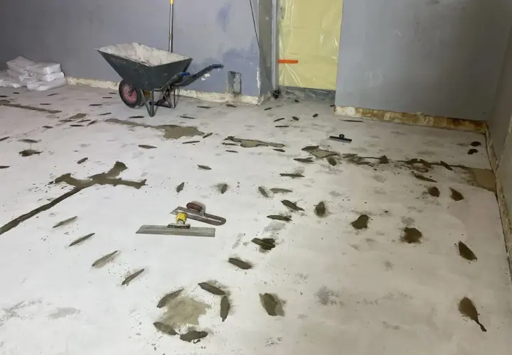 Arbetsplats för att laga betonggolv. Skottkärra, säckar med material och verktyg ligger redo.