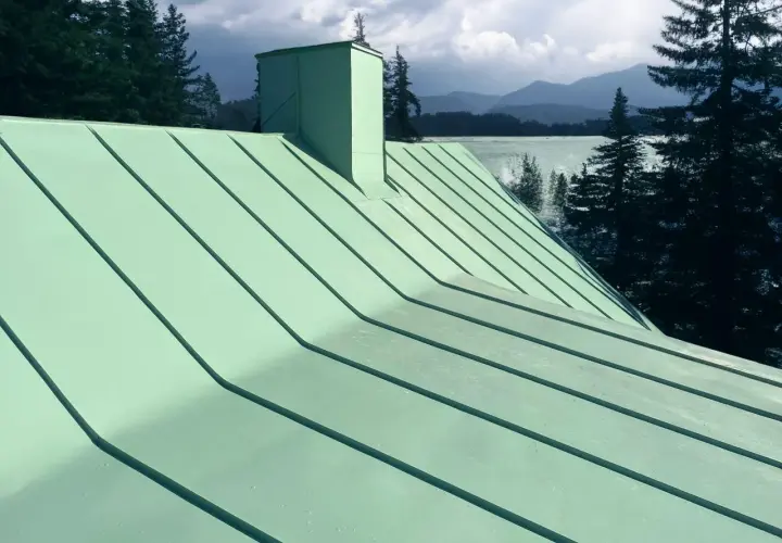 Grönt plåttak med skorsten, vacker utsikt över sjö och berg. Tänk på kostnad plåttak vid renovering.