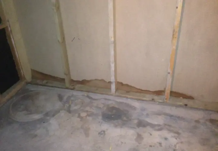 Synlig fukt i garage vid golvet och längs väggen. Vattenfläckar på betongen och mörka märken på väggens nederkant.