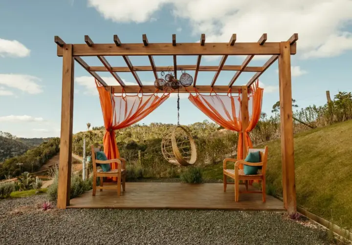 En träpergola med orange draperier och hängstol. Perfekt för avkoppling, kanske efter att ha fått pergola bygglov.