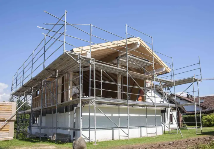 Bygga på en våning: Ställningar omger ett hus under ombyggnad, med synliga träbjälkar och takkonstruktion.
