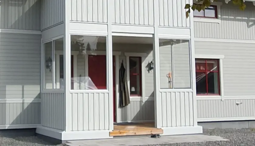 Nybyggd farstukvist med vita träpaneler och glaspartier. En röd ytterdörr syns innanför.