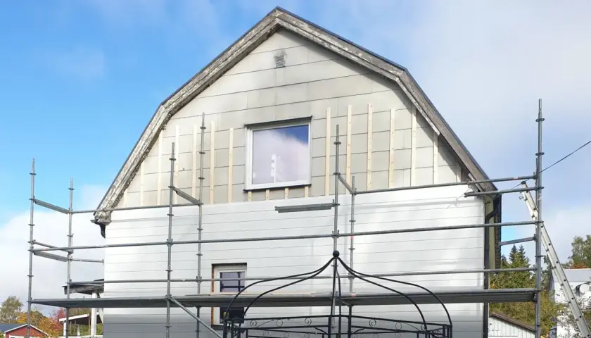 Hus med eternit fasad under renovering, ställningar uppsatta.