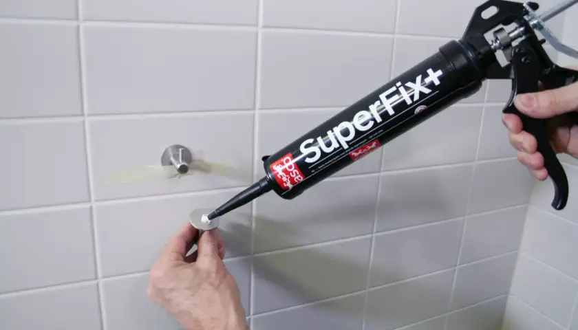 En hand använder en fogpistol med "SuperFix+" för att limma kakel. En metallbricka med ett fäste är redo att monteras.