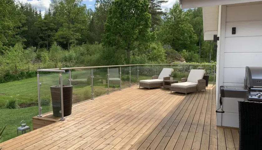 En vacker altan med olja trall, solstolar och grill. Omgiven av grönskande natur.