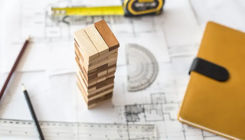 Ritningar, måttband, pennor och en Jenga-torn som symboliserar planeringen för att renovera garage.