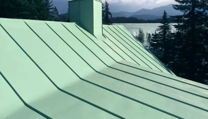 Grönt plåttak med skorsten, vacker utsikt över sjö och berg. Tänk på kostnad plåttak vid renovering.