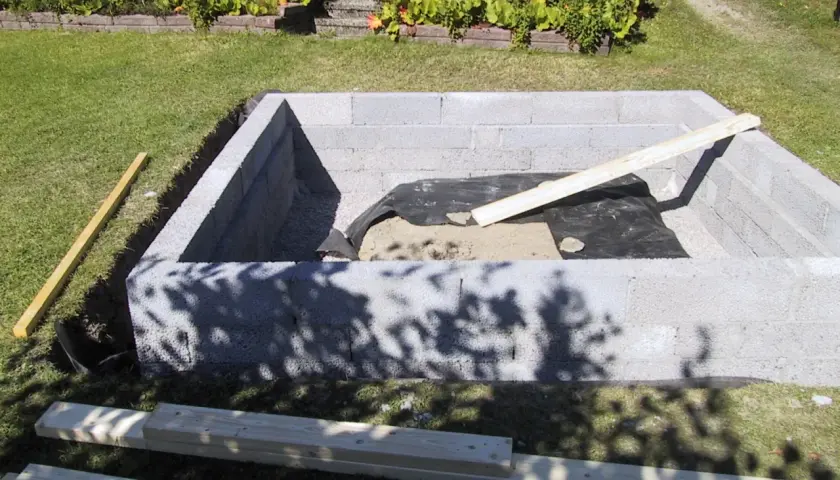 Byggnation av en grund med lecablock. Grus och markduk ligger på plats. Träreglar ligger redo för användning.