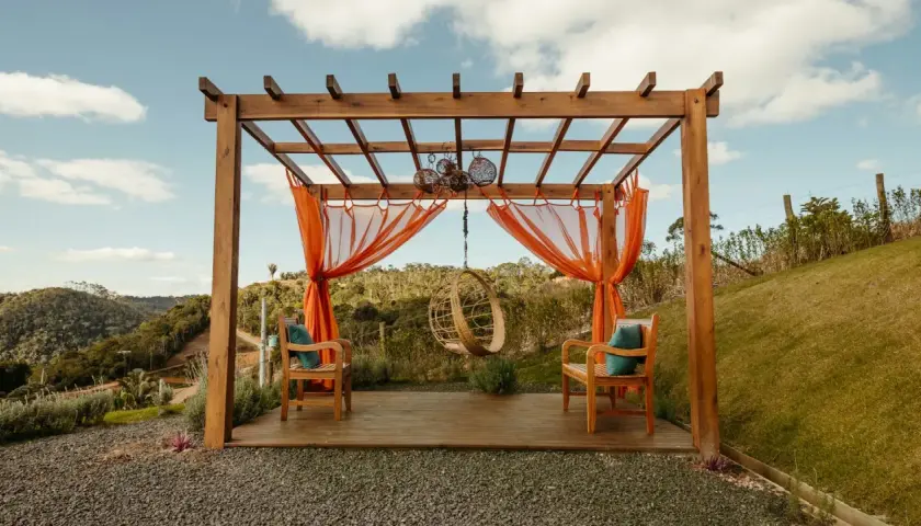 En träpergola med orange draperier och hängstol. Perfekt för avkoppling, kanske efter att ha fått pergola bygglov.