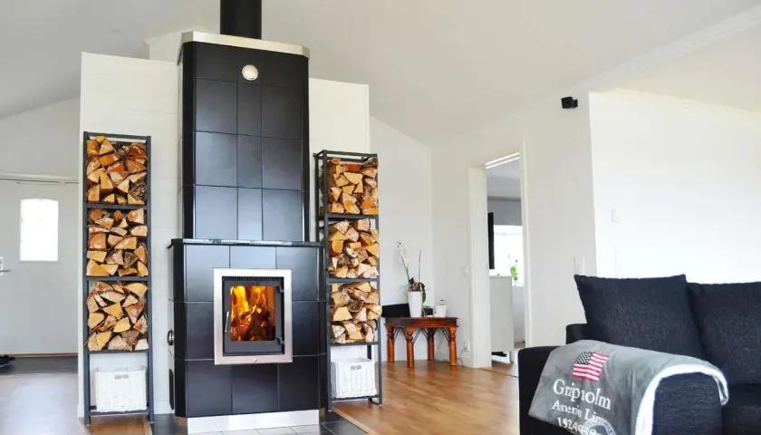 En modern kamin i uterummet med ved i staplar på sidorna. En mysig plats att värma sig vid.