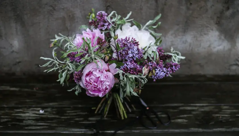 En bukett med rosa pioner, vita pioner och lila syren. Vackra snittblommor sorter som ser ut att vara nyss plockade.