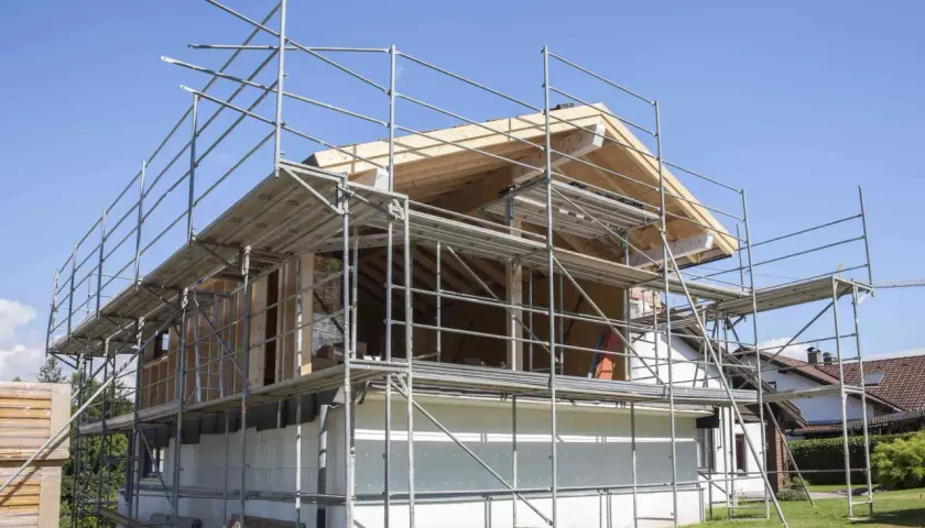 Bygga på en våning: Ställningar omger ett hus under ombyggnad, med synliga träbjälkar och takkonstruktion.