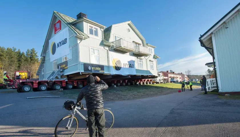 Ett stort hus är på väg att flytta. En man med cykel stannar för att titta på det imponerande arbetet.