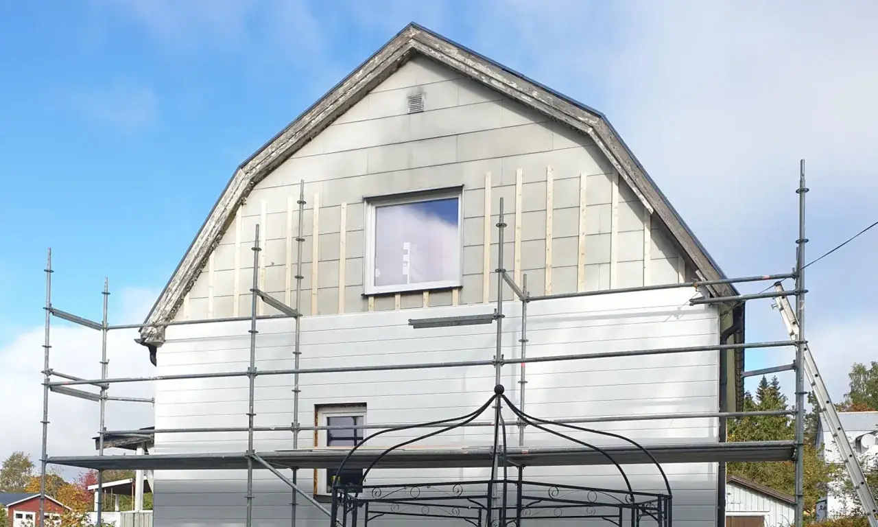 Hus med eternit fasad under renovering, ställningar uppsatta.