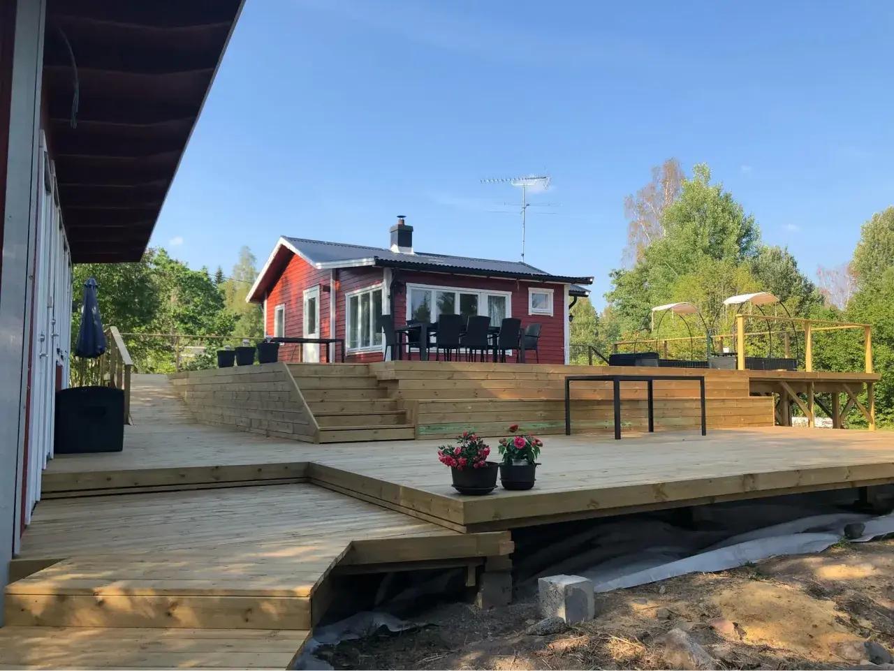 Stor altan i trä med trappor och sittgrupp framför rött hus. Perfekt altan inspiration för sommarens grillkvällar.