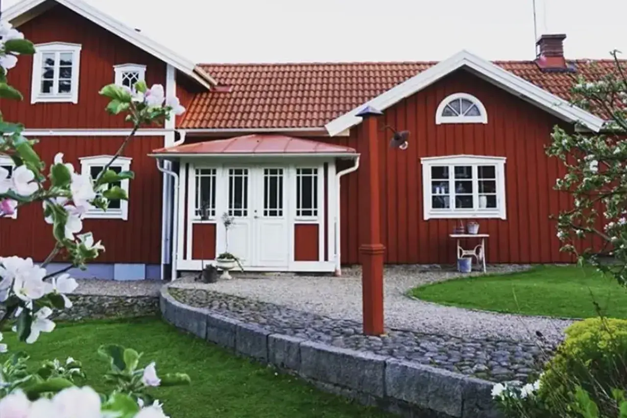 Rött hus med vita fönster och dörrar, en vacker trädgård med blommande träd. Planer på att bygga ut gammalt hus syns inte, men det ser ut som ett drömhem.