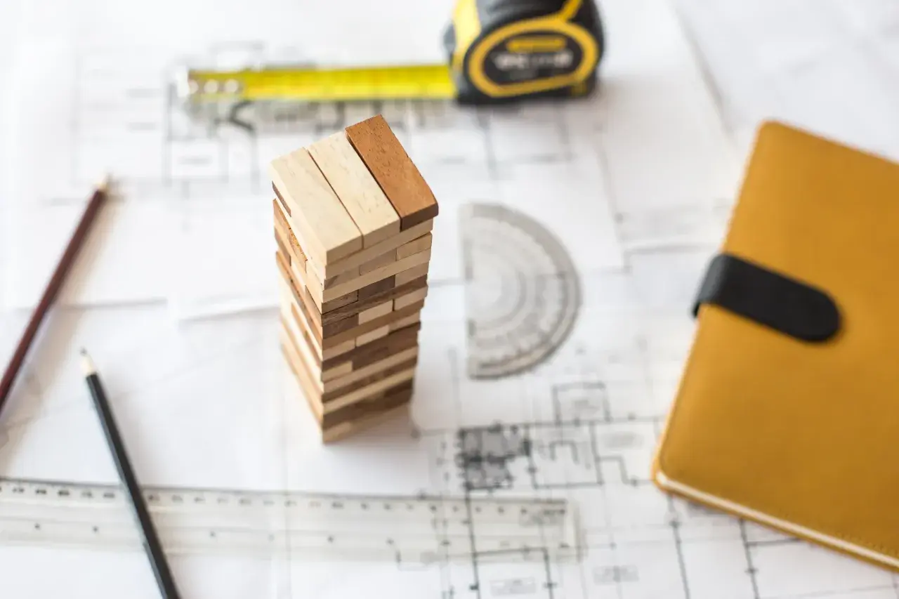 Ritningar, måttband, pennor och en Jenga-torn som symboliserar planeringen för att renovera garage.