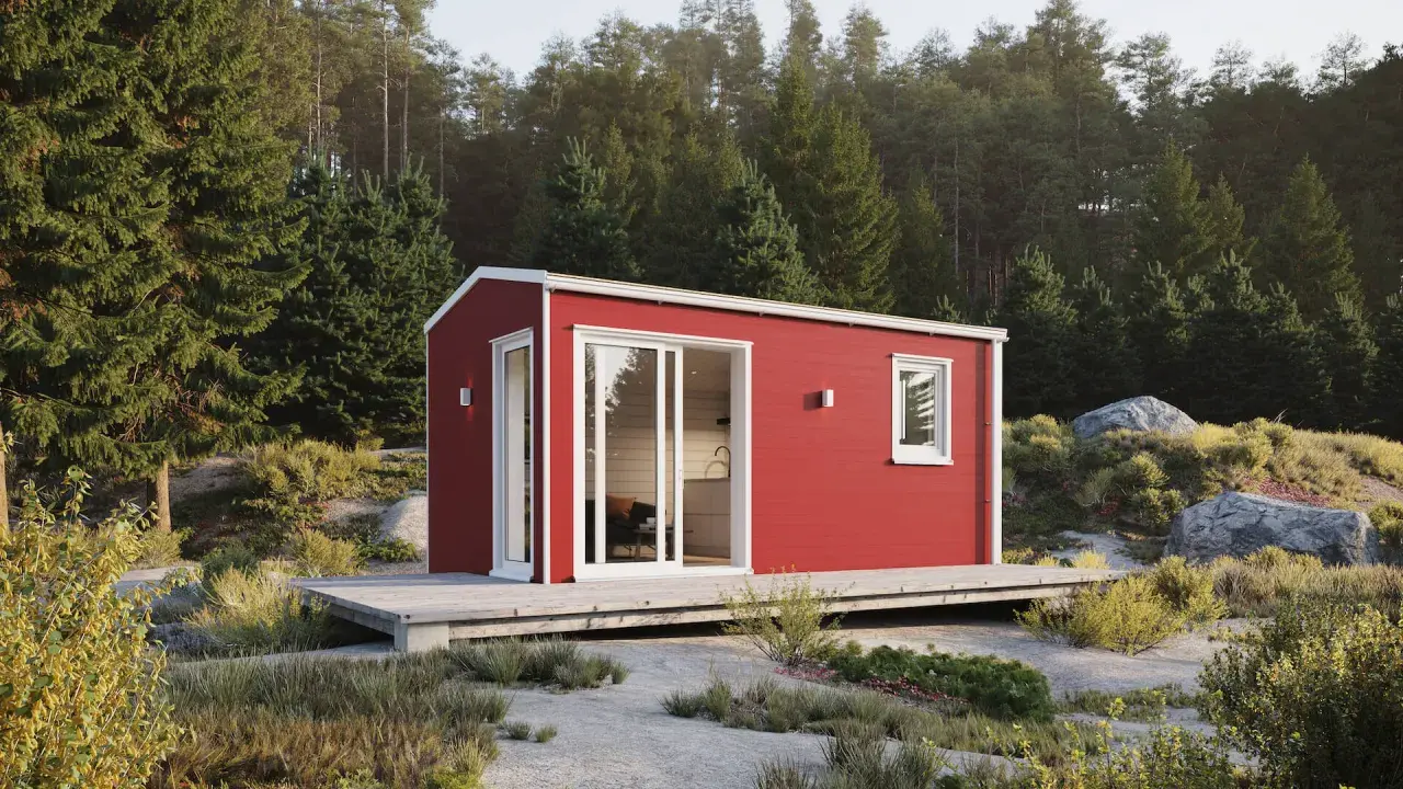 Röd friggebod med stora fönster och altan, placerad i en skogsglänta. Perfekt för dig som vill flytta friggebod och skapa en egen oas.