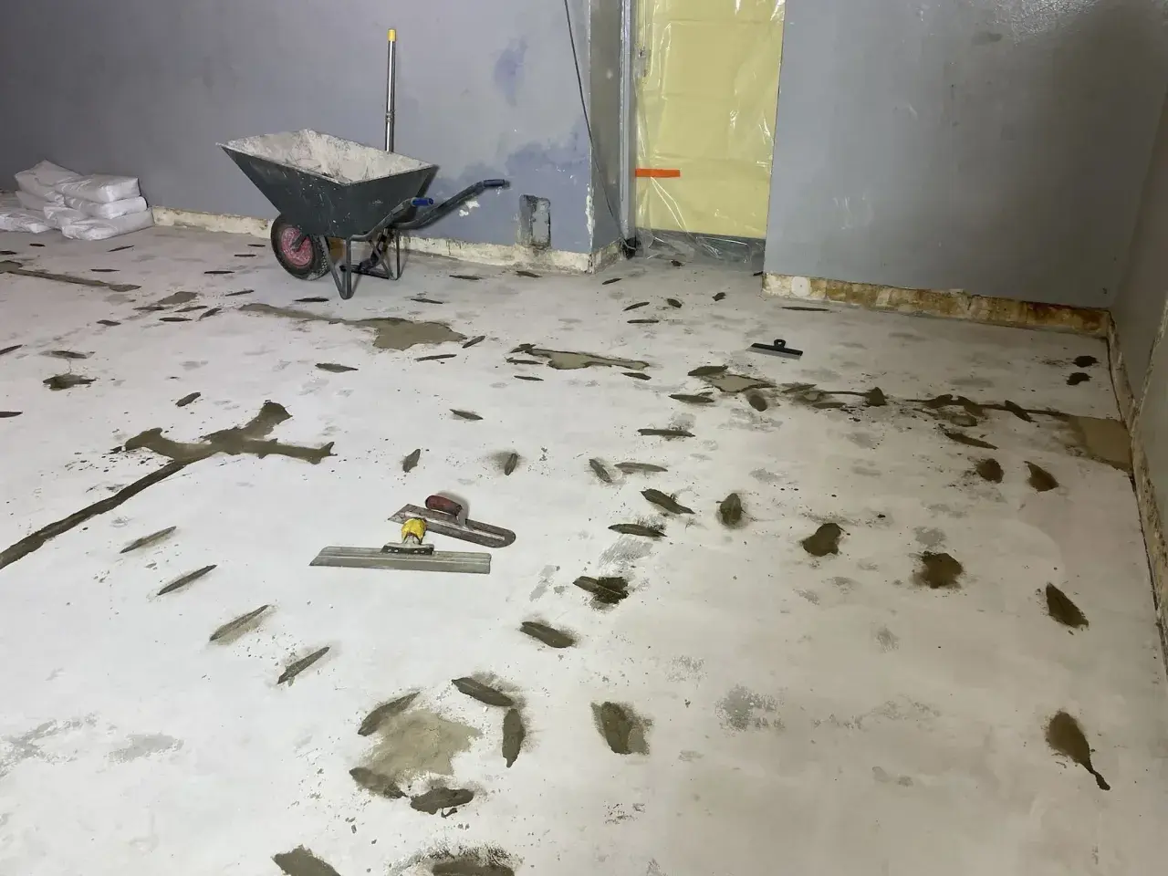 Arbetsplats för att laga betonggolv. Skottkärra, säckar med material och verktyg ligger redo.