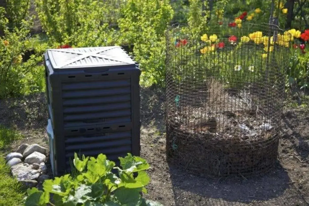 En svart kompostbehållare och en rund kompost av nät står i en trädgård. En bra plats att börja bygga varmkompost.