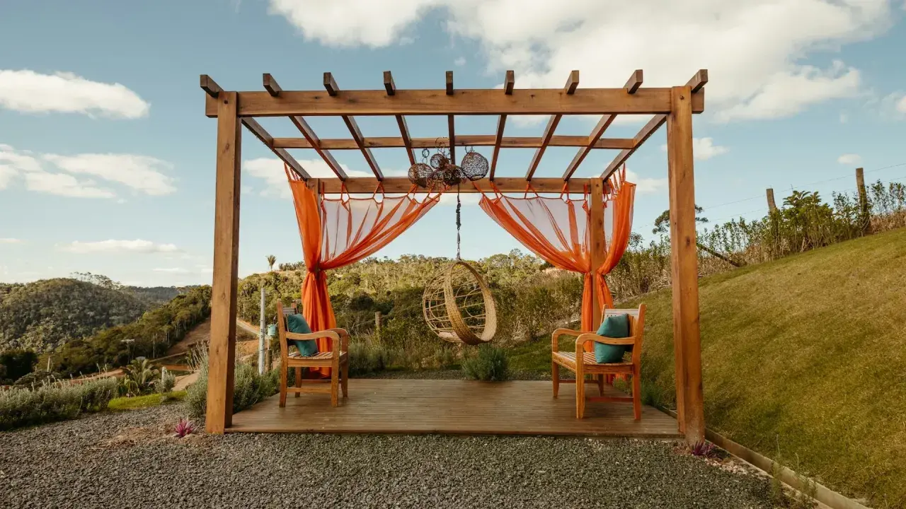 En träpergola med orange draperier och hängstol. Perfekt för avkoppling, kanske efter att ha fått pergola bygglov.