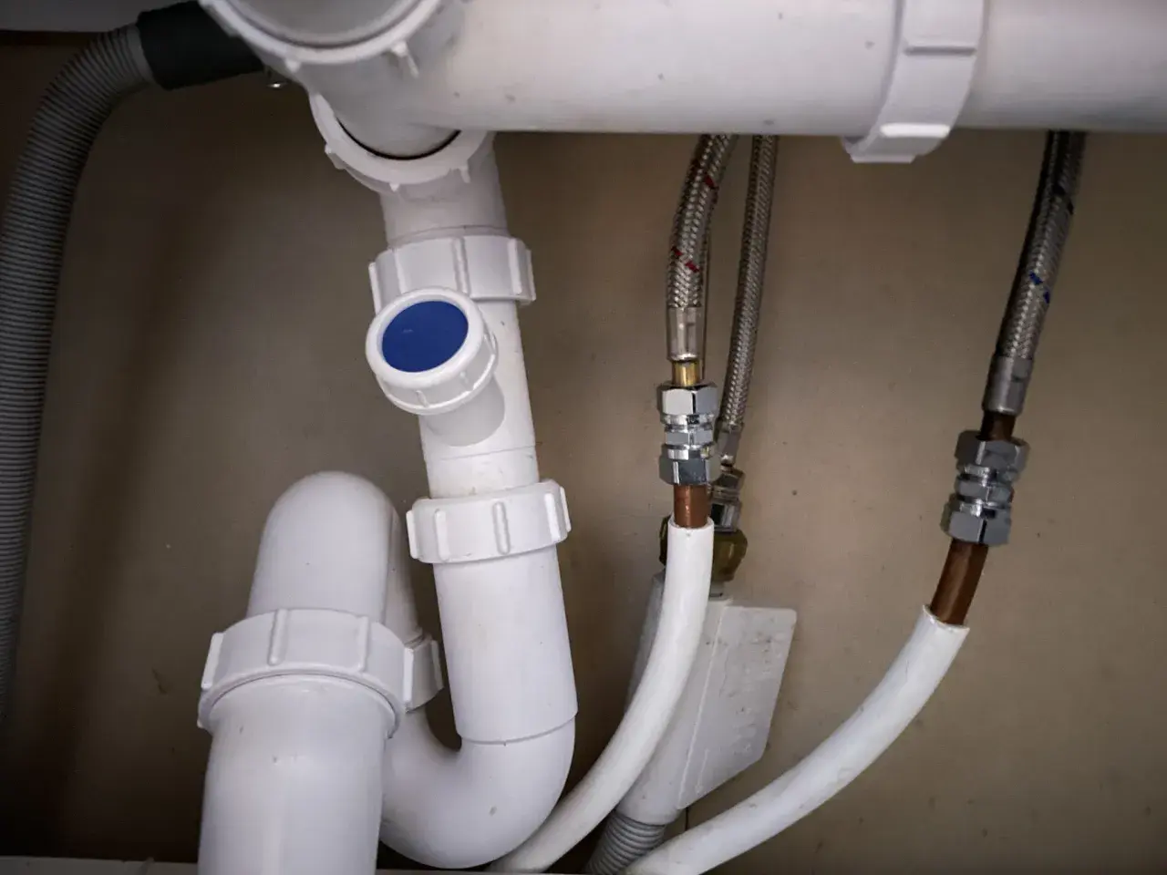 Detaljerad vy av avloppsrör med en blå topp, troligen en vakuumventil avlopp placering. Flexibla slangar ansluter till vattenledningar.
